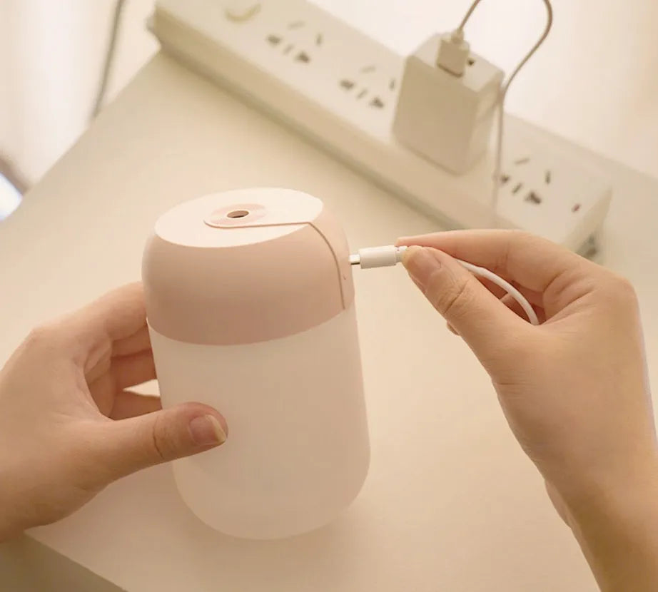 White cylindrical mini humidifier with USB cable and aromatherapy tray on a wooden desk.