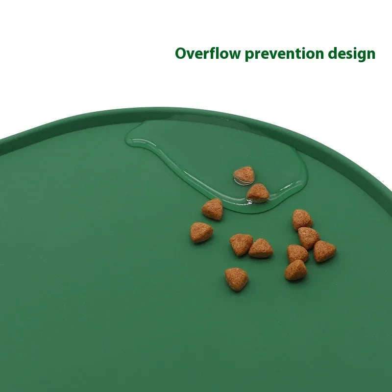 Green silicone cat feeding mat with raised edge containing a food bowl and scattered kibble on a kitchen floor.