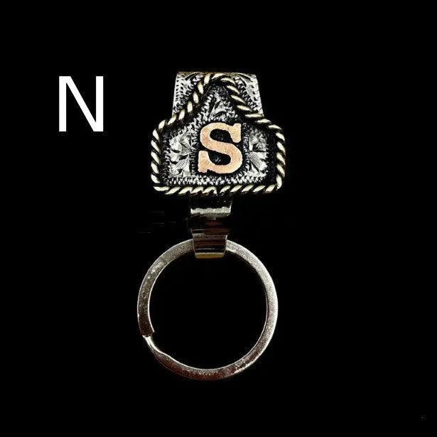 Handmade metal cow tag belt keychain showing one of 26 colour options, each marked with a different alphabet letter.