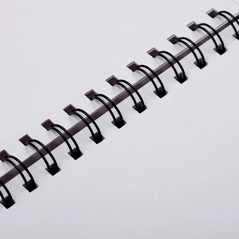 A sketchbook open on a table, showing coil binding and heavy-weight paper suitable for drawing.