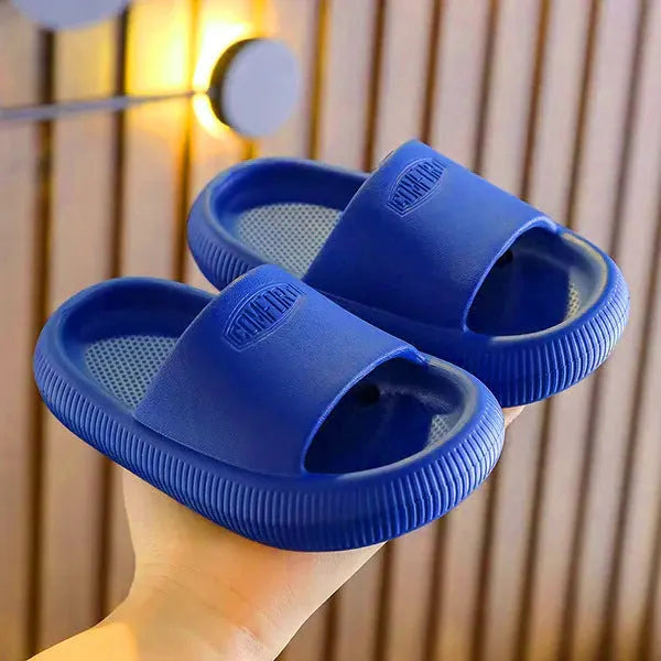 A pair of bright blue, one-piece EVA children's slippers with a textured non-slip sole, shown on a wooden floor.