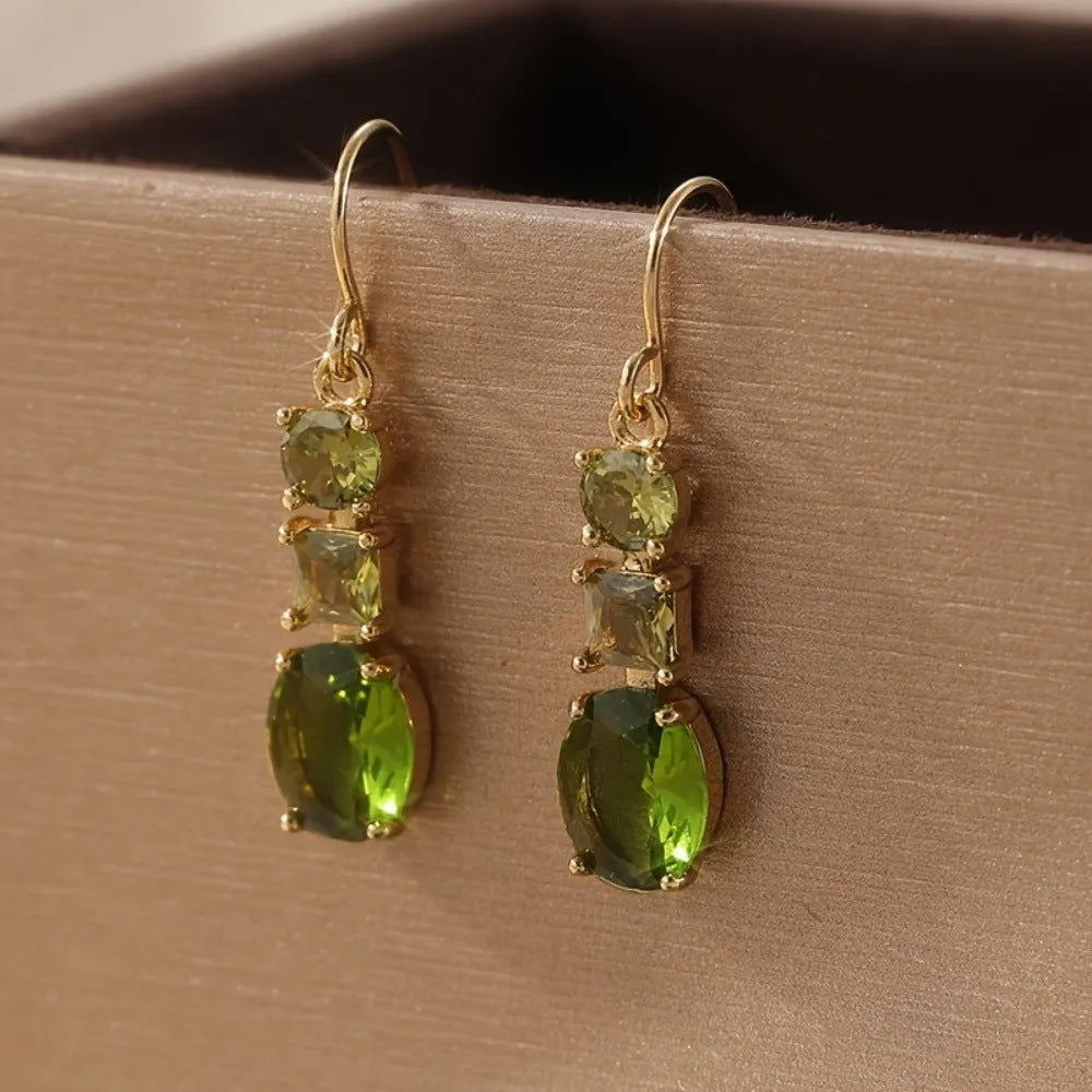 Green geometric copper earrings with a quadrilateral shape on a plain background.
