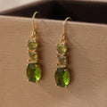 Green geometric copper earrings with a quadrilateral shape on a plain background.