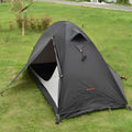 Red single person backpacking tent with aluminium poles pitched in a forest, showing double-layer design and vestibule.