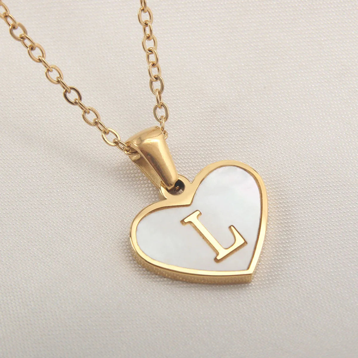 Gold-plated heart necklace with white shell pendant showing initial engraving on stainless steel chain