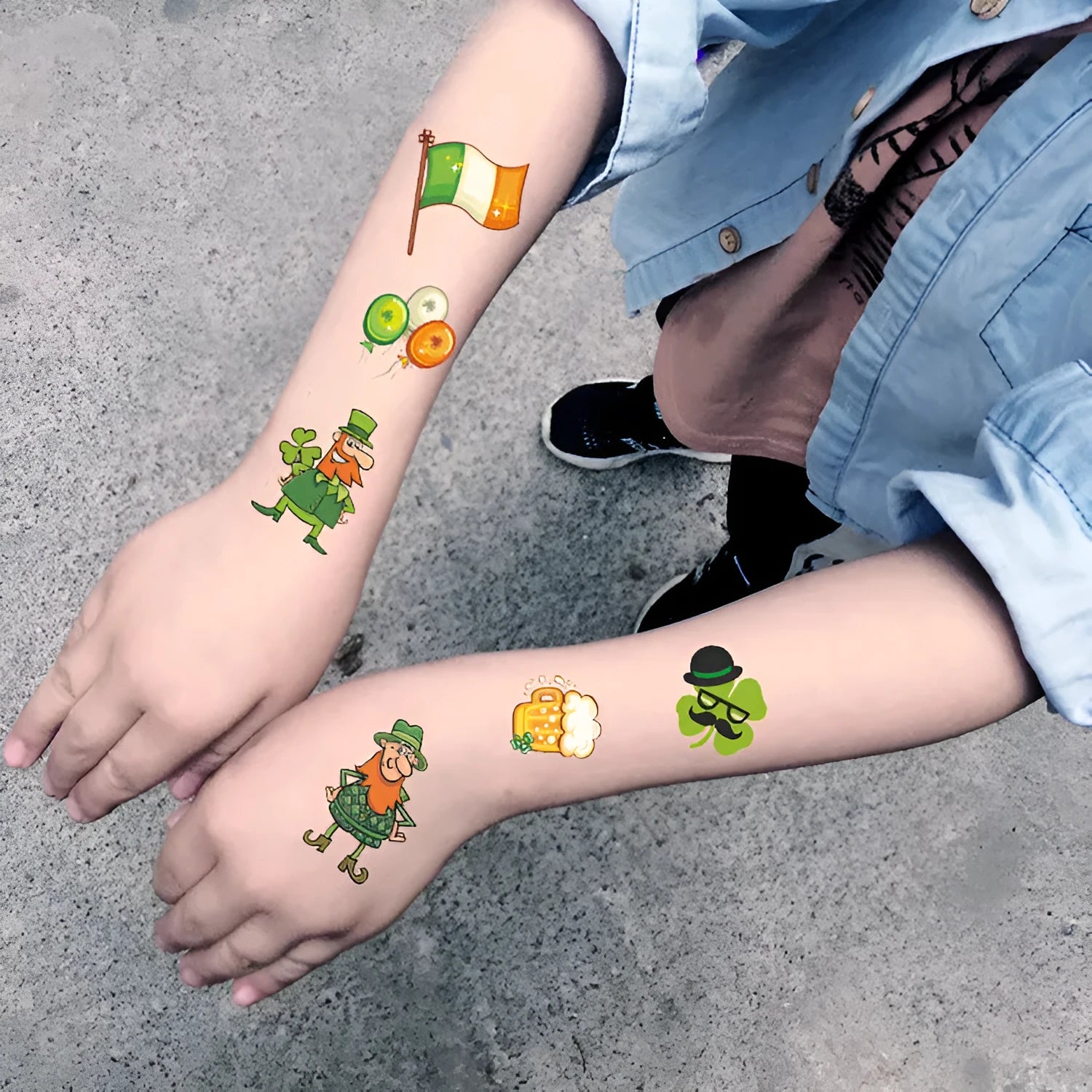A single sheet of tattoo sticker paper featuring a green cartoon clover design for St. Patrick's Day, showing the water-transfer backing.