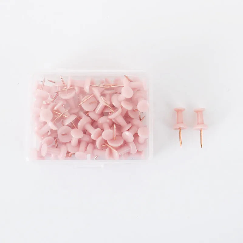 Morandi colour push pins in green, grey, and pink with three different head designs on cork board