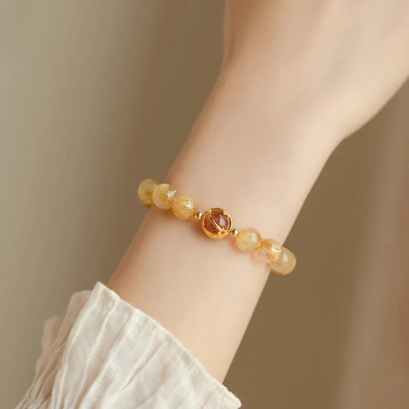 Citrine gold rutilated quartz crystal bracelet with diamond-cut beads on a wrist.