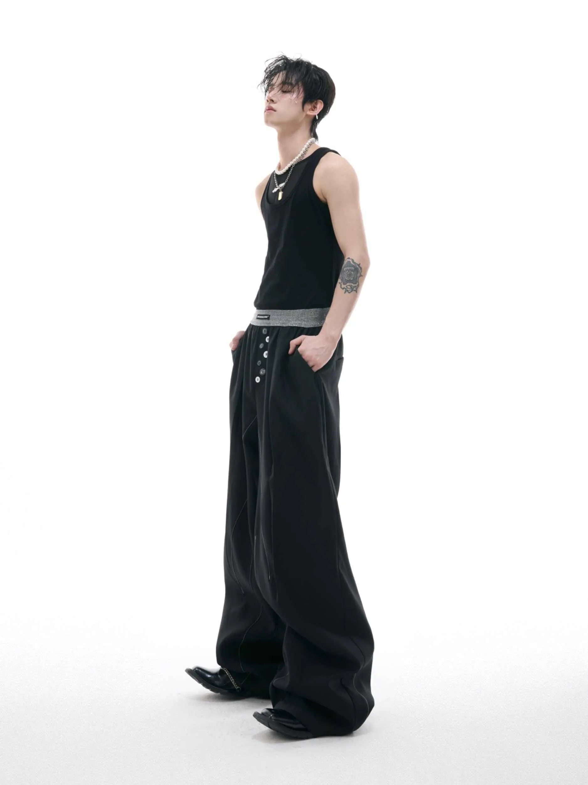 Straight-leg high-waisted trousers in black with a drooping waistband and button detail on a neutral background.