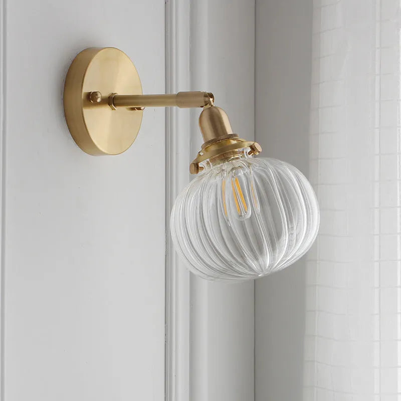 Close-up of a hand-blown pumpkin-shaped glass wall lamp in blue, mounted on a beige wall.