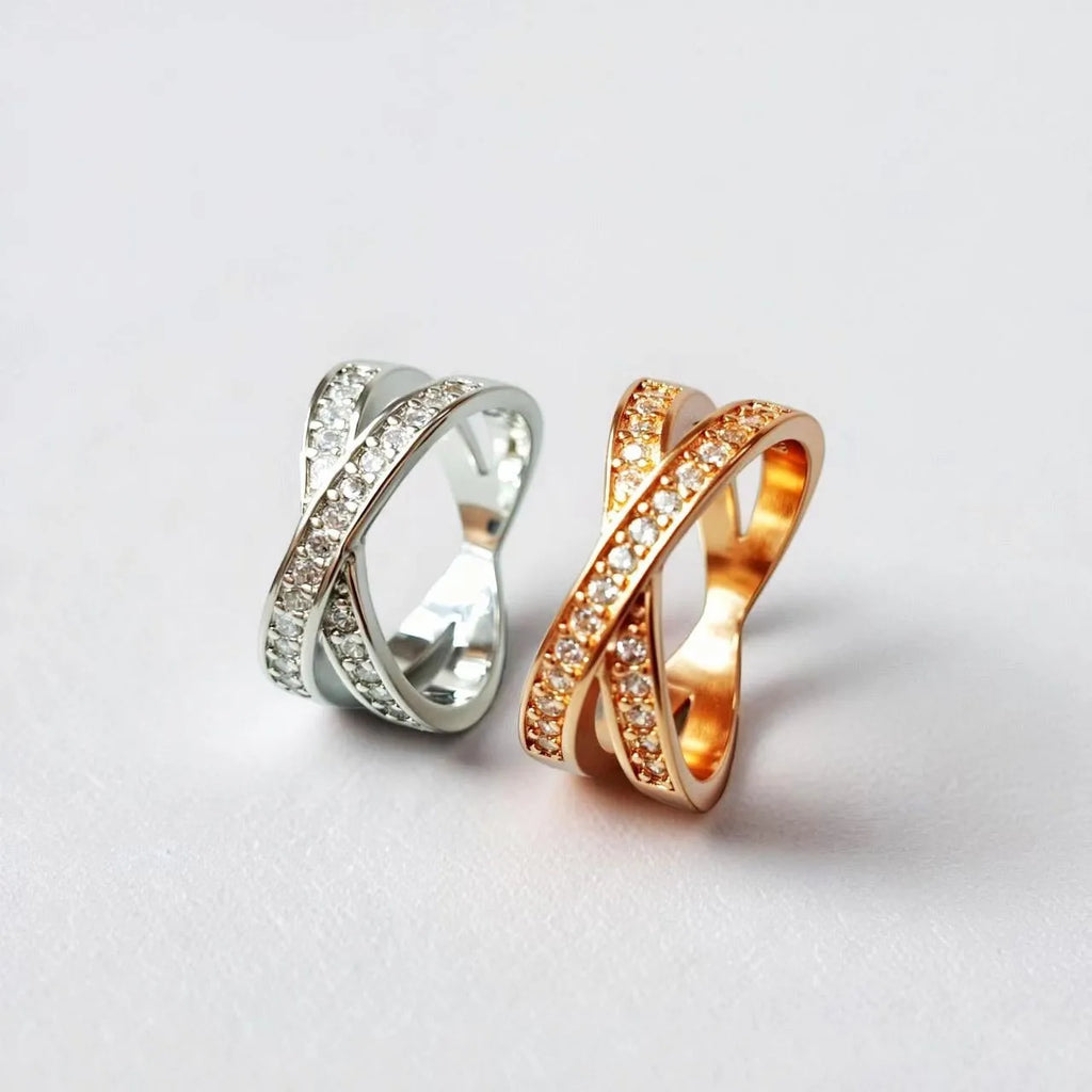 A geometric silver cross ring with small zircon stones on a person's hand, showing a simple band design.