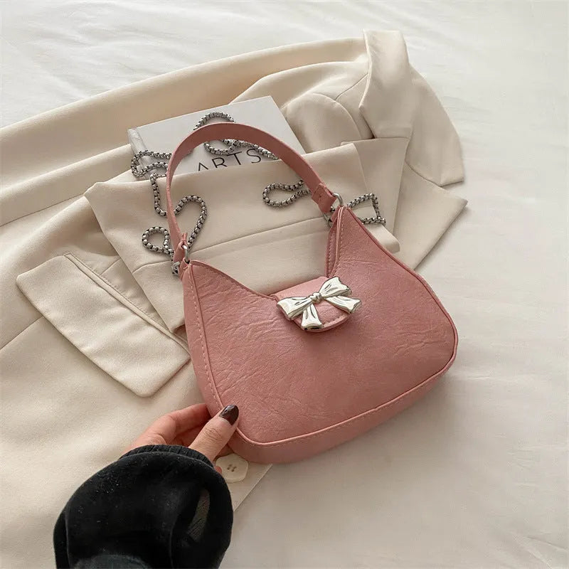 Bow underarm bag in textured PU with one-shoulder strap, dumpling shape and sandwich pocket, shown in black, pink, silver or white