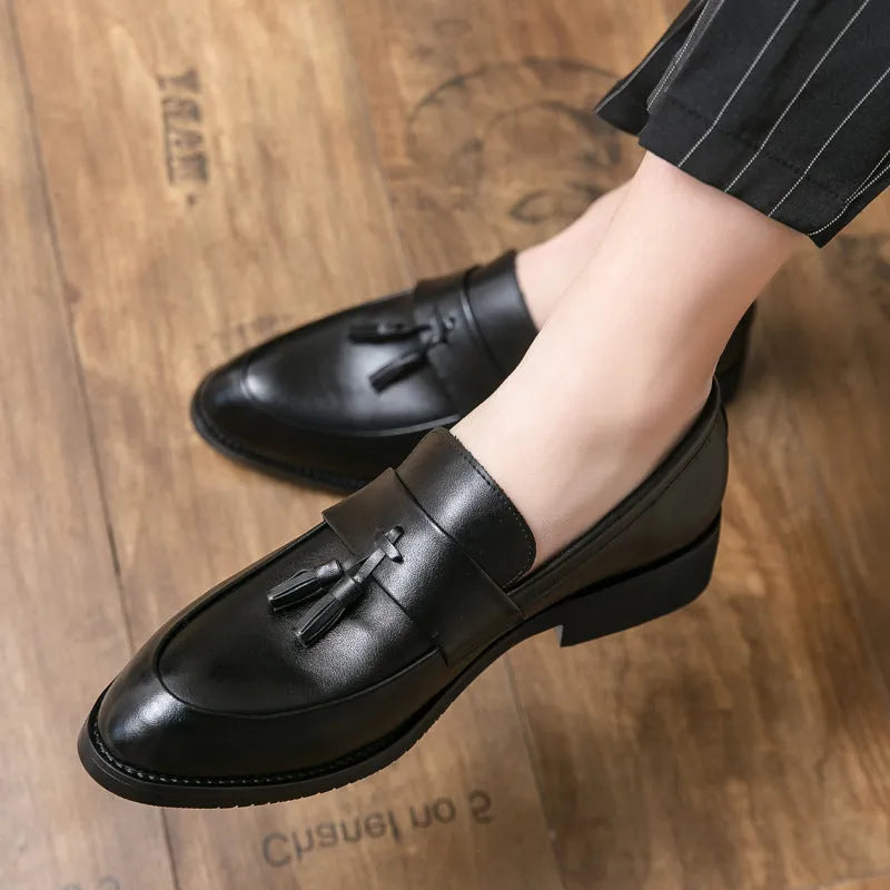 Men's black slip-on business casual shoes with a tassel detail and pointed toe on a rubber sole.