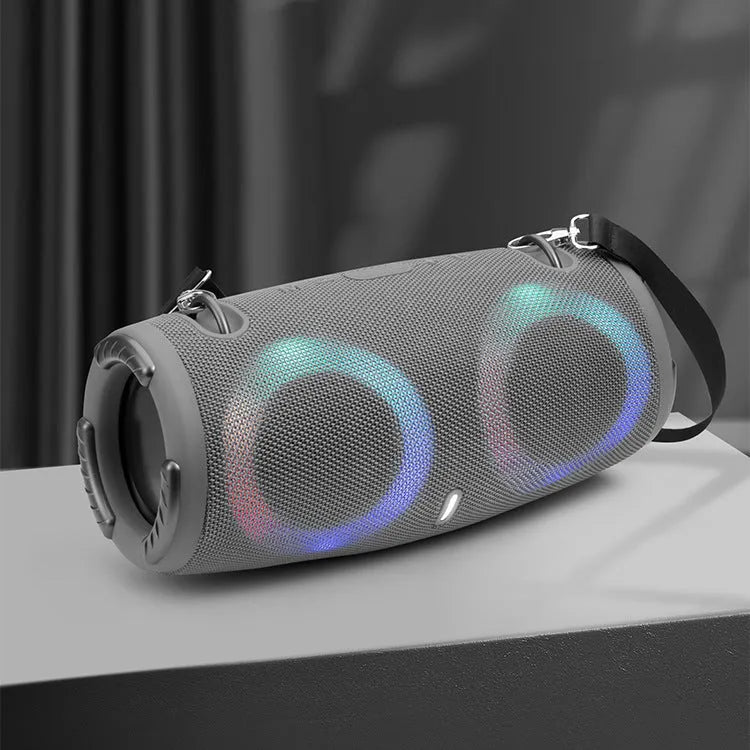 Cylindrical War Drum Bluetooth speaker with glowing RGB lights, a black metal grille, and a carrying strap on a wooden table.