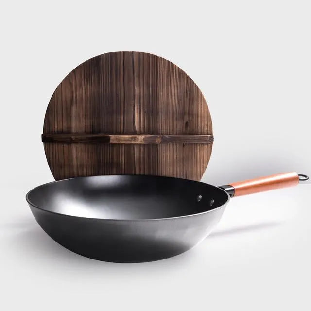 Black traditional cast iron wok with a long wooden handle on a kitchen counter.