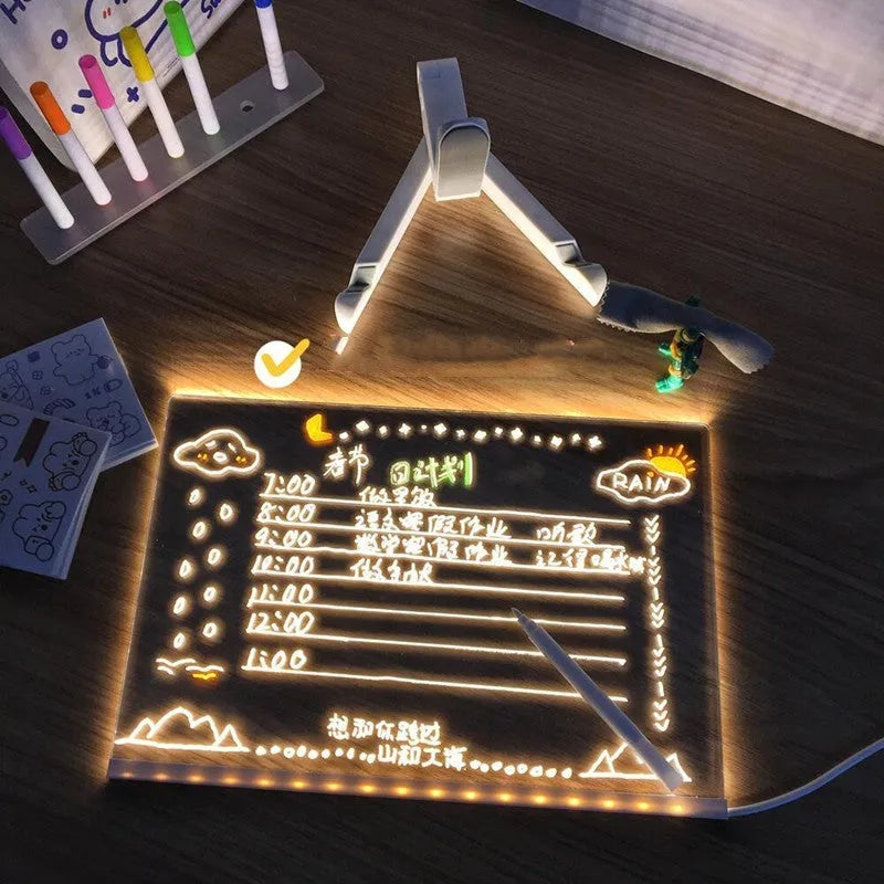 DIY acrylic message board LED night light on desk with colourful writing, USB cable, and pens