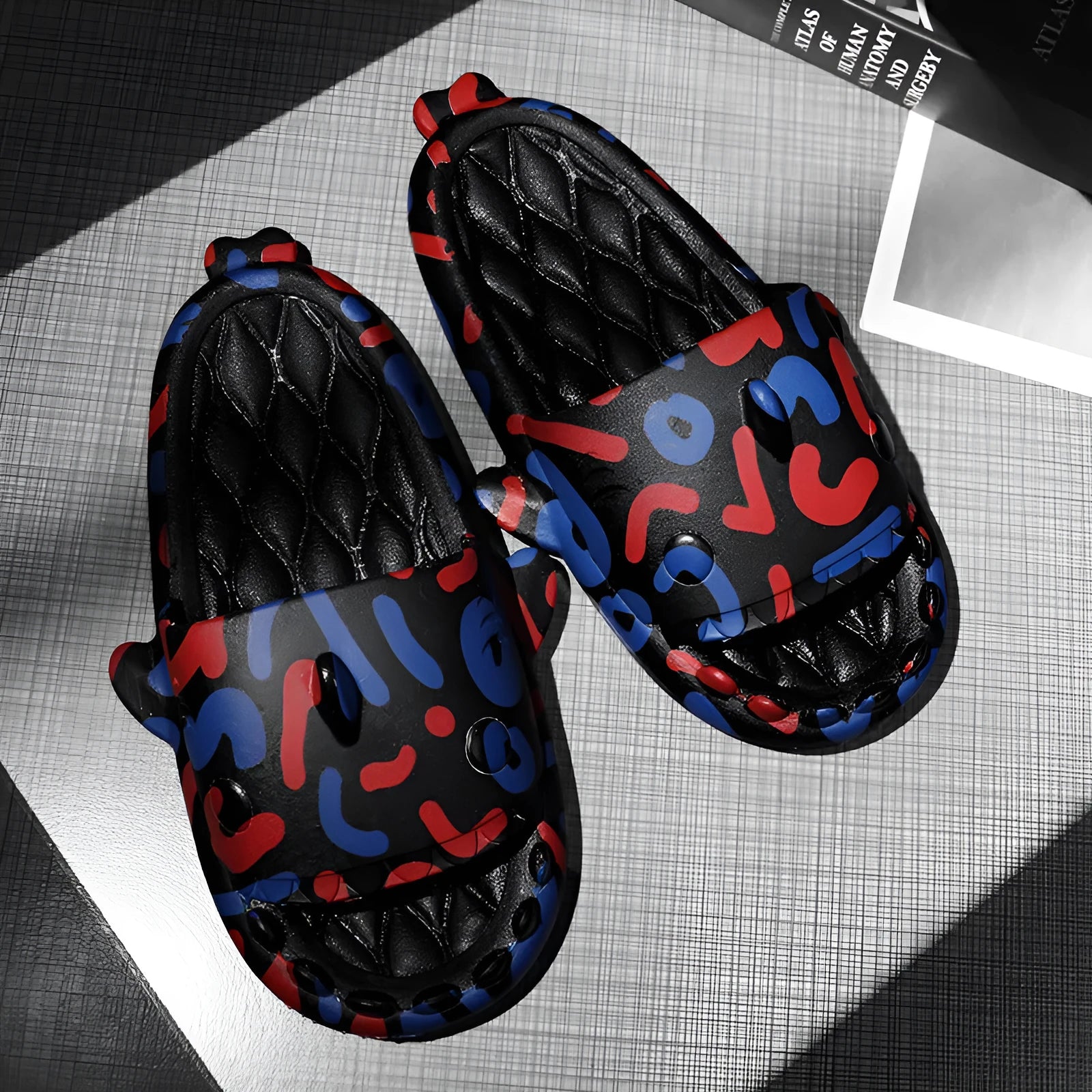 Pair of grey open-toe EVA slippers with raised shark design on the front, shown on a wooden floor.