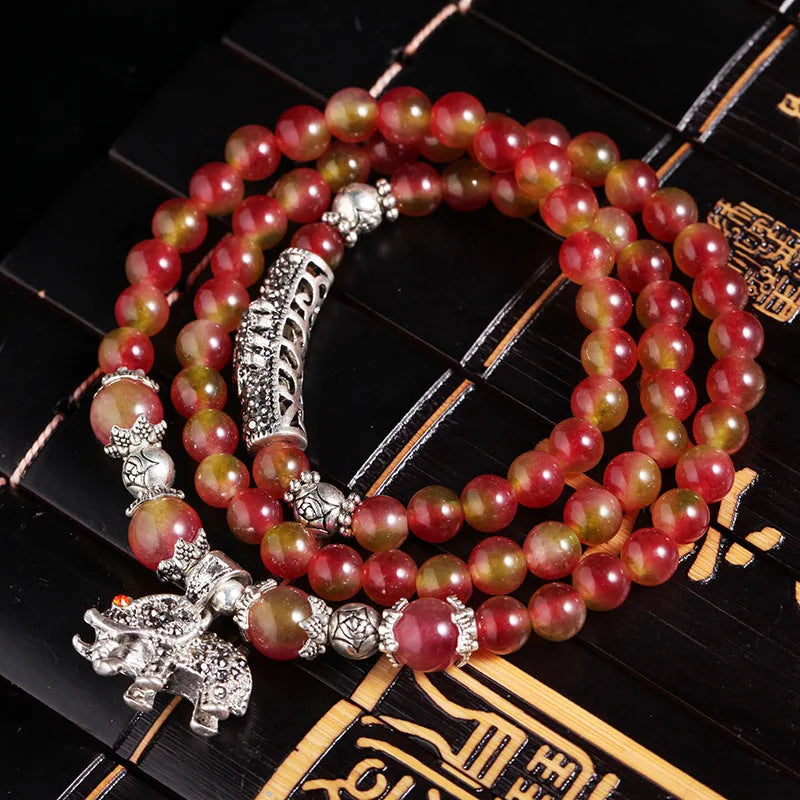 A handmade bracelet with geometrically cut watermelon crystal beads and a red Chinese knot closure on a white background.