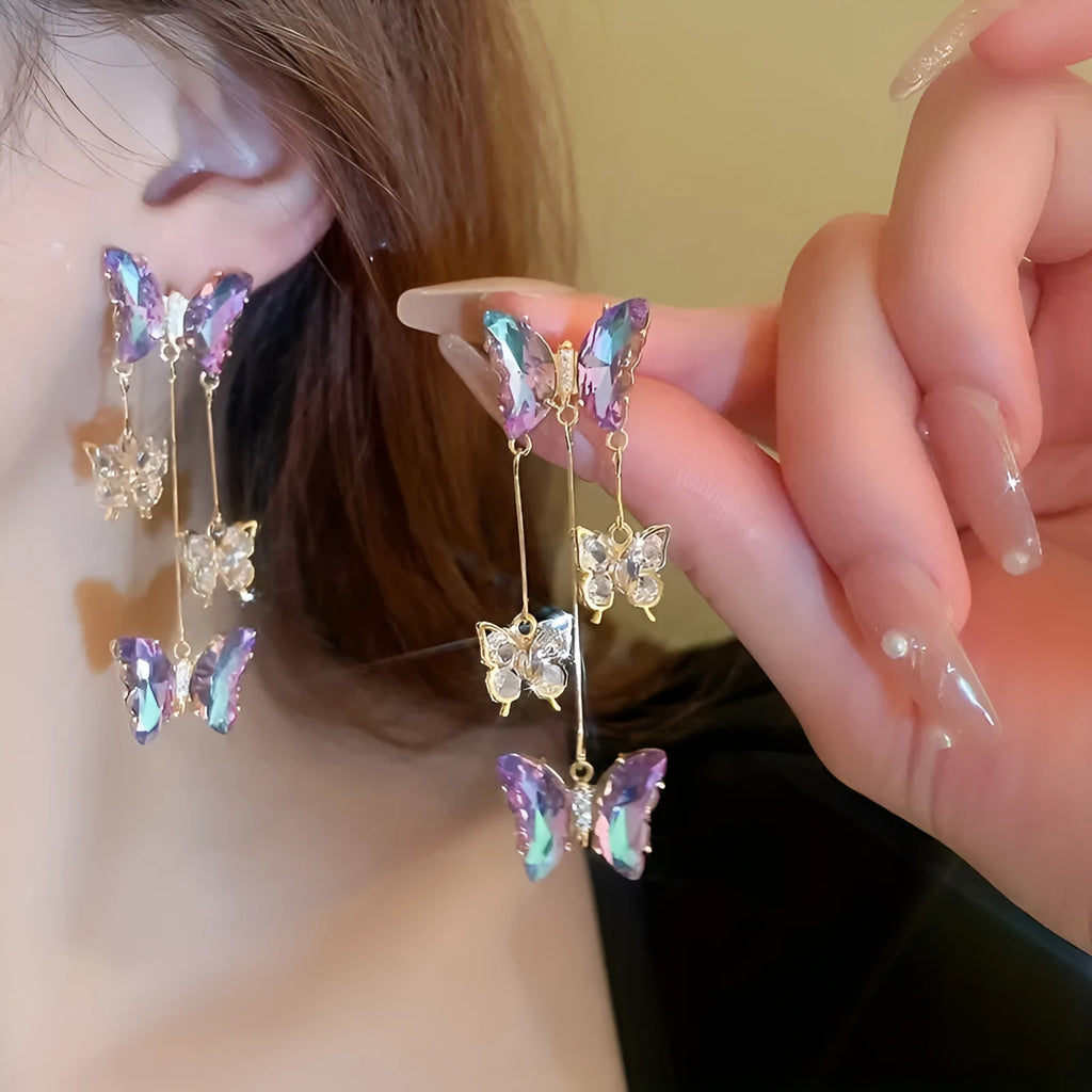 Long silver drop earrings with a blue-purple butterfly, crystal flowers, and a delicate tassel on a white background.