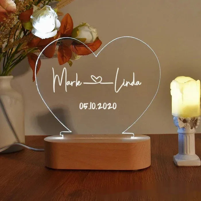 Custom transparent acrylic night light with engraved names and date, lit by an LED base on a table.