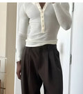 A cream-coloured men's ribbed long-sleeve henley top with a buttoned placket on a hanger.