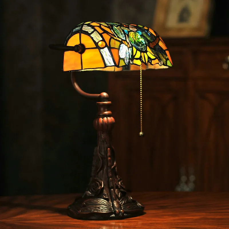 Tiffany style table lamp with colourful stained glass shade and resin base on a wooden table.