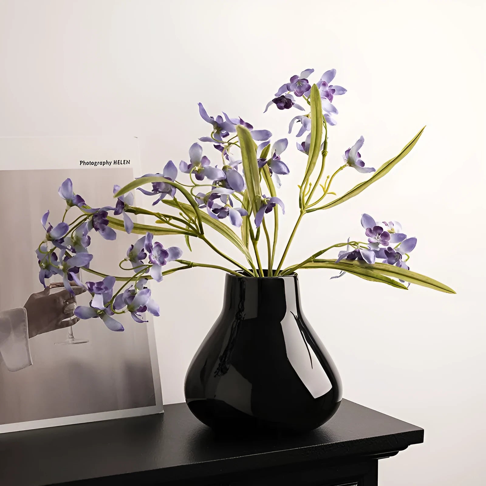 Modern round belly ceramic vase with coloured glaze, shown in black and white, some with artificial flowers.