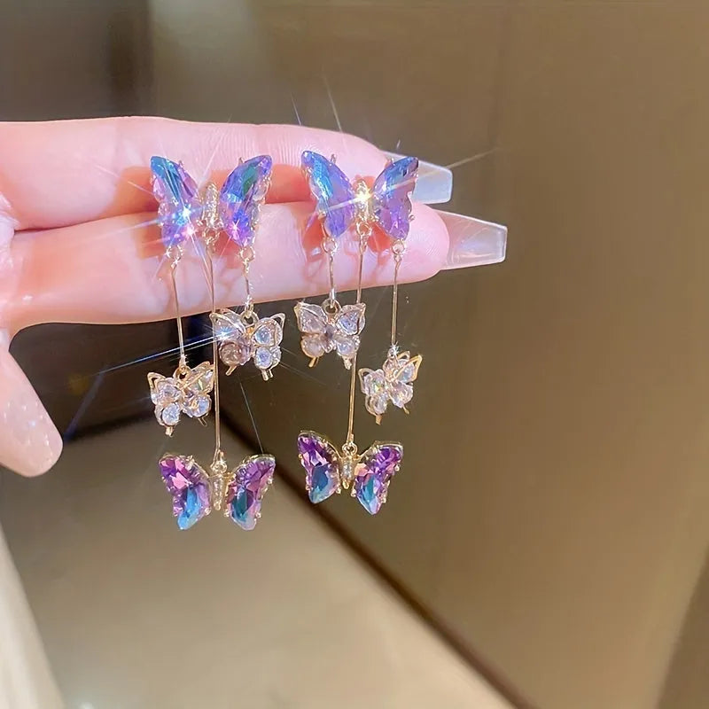Long silver drop earrings with a blue-purple butterfly, crystal flowers, and a delicate tassel on a white background.