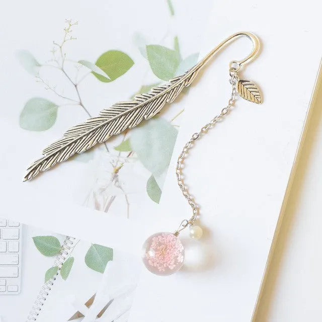 Close-up of a metal alloy bookmark with real dried pink flowers sealed inside, on an open book.