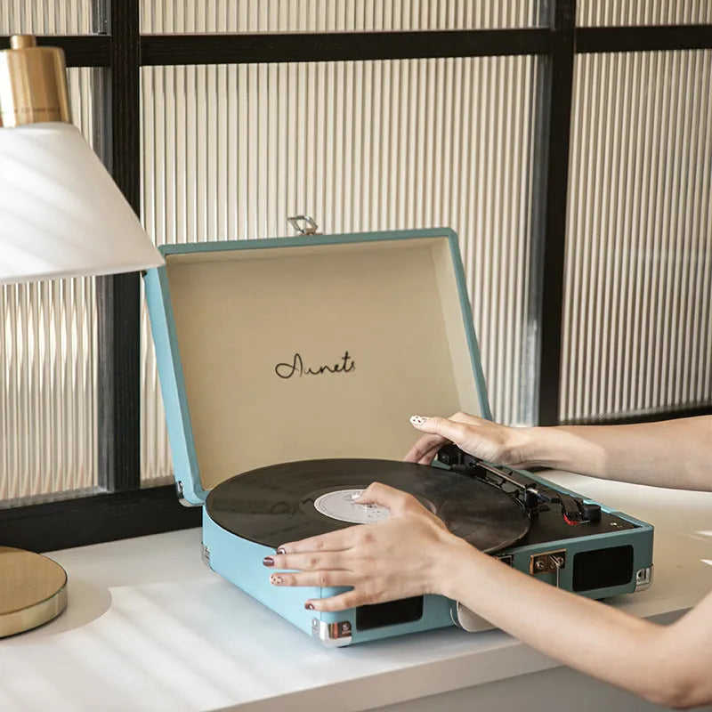 Cream-coloured retro phonograph in leather-effect suitcase with record on turntable and handle visible