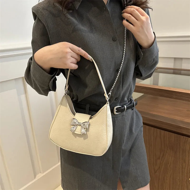 Bow underarm bag in textured PU with one-shoulder strap, dumpling shape and sandwich pocket, shown in black, pink, silver or white