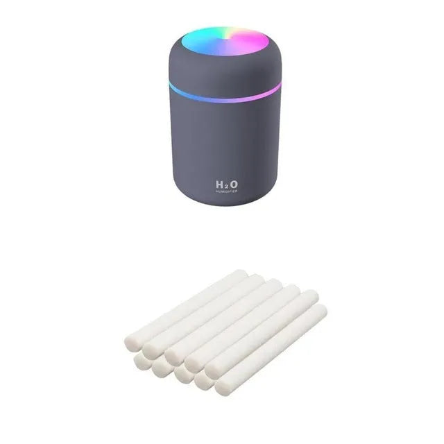 Pink USB mini humidifier with LED lights on wooden desk beside laptop