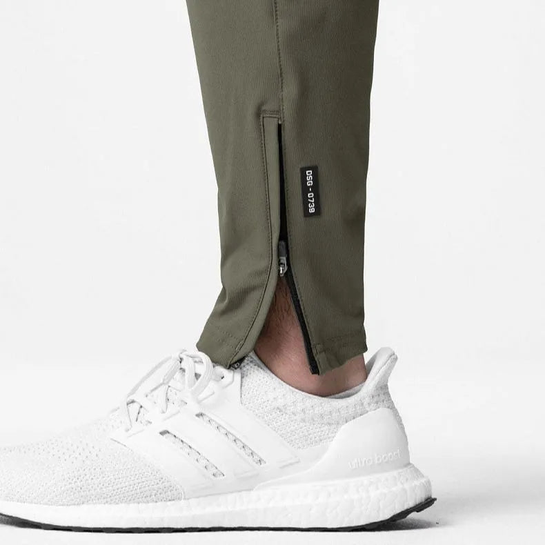 Man wearing dark grey loose-fit fitness trousers with tied ankles, made of quick-dry polyester blend fabric.