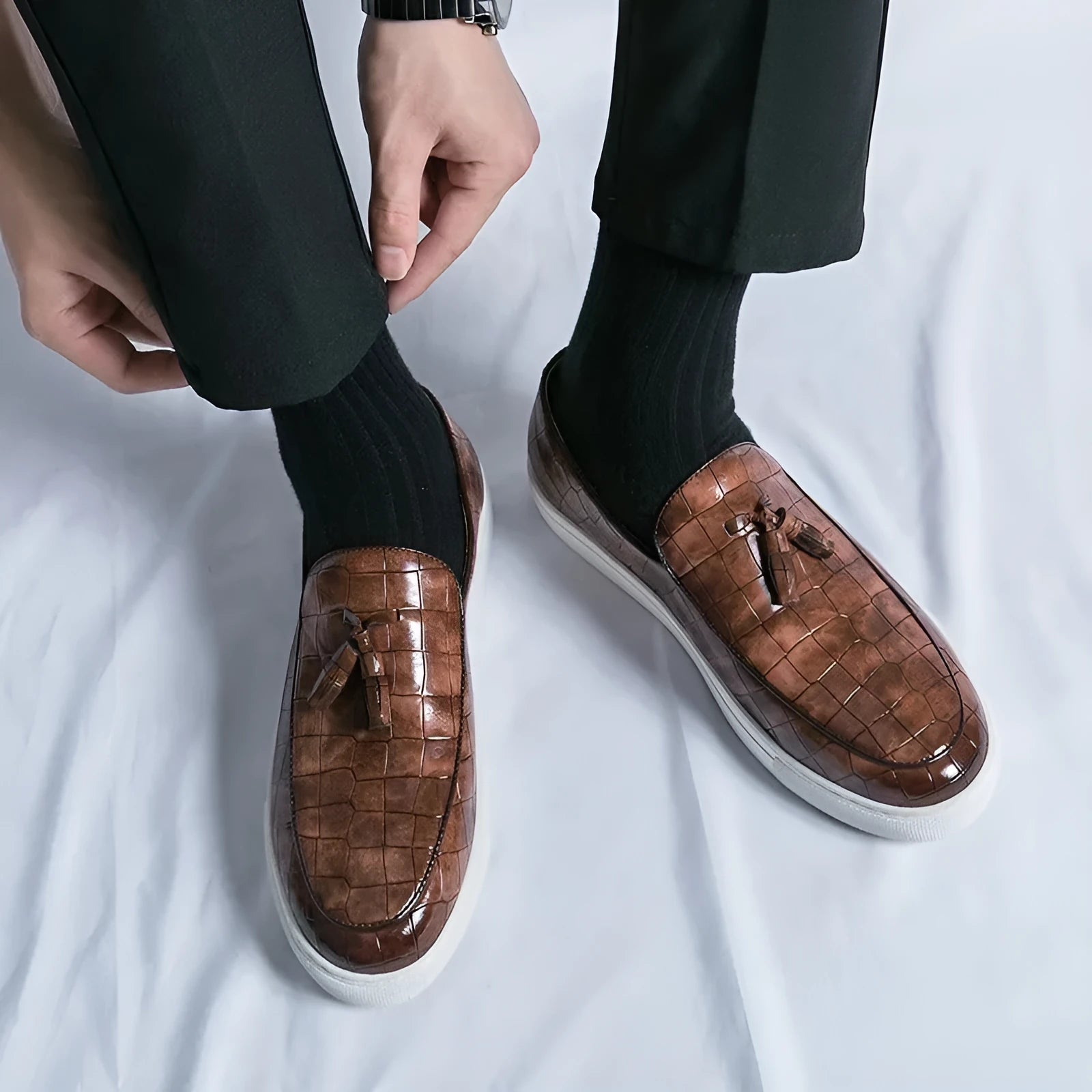 Men's black leather sneakers with a tassel detail on a round toe, shown on a white background.