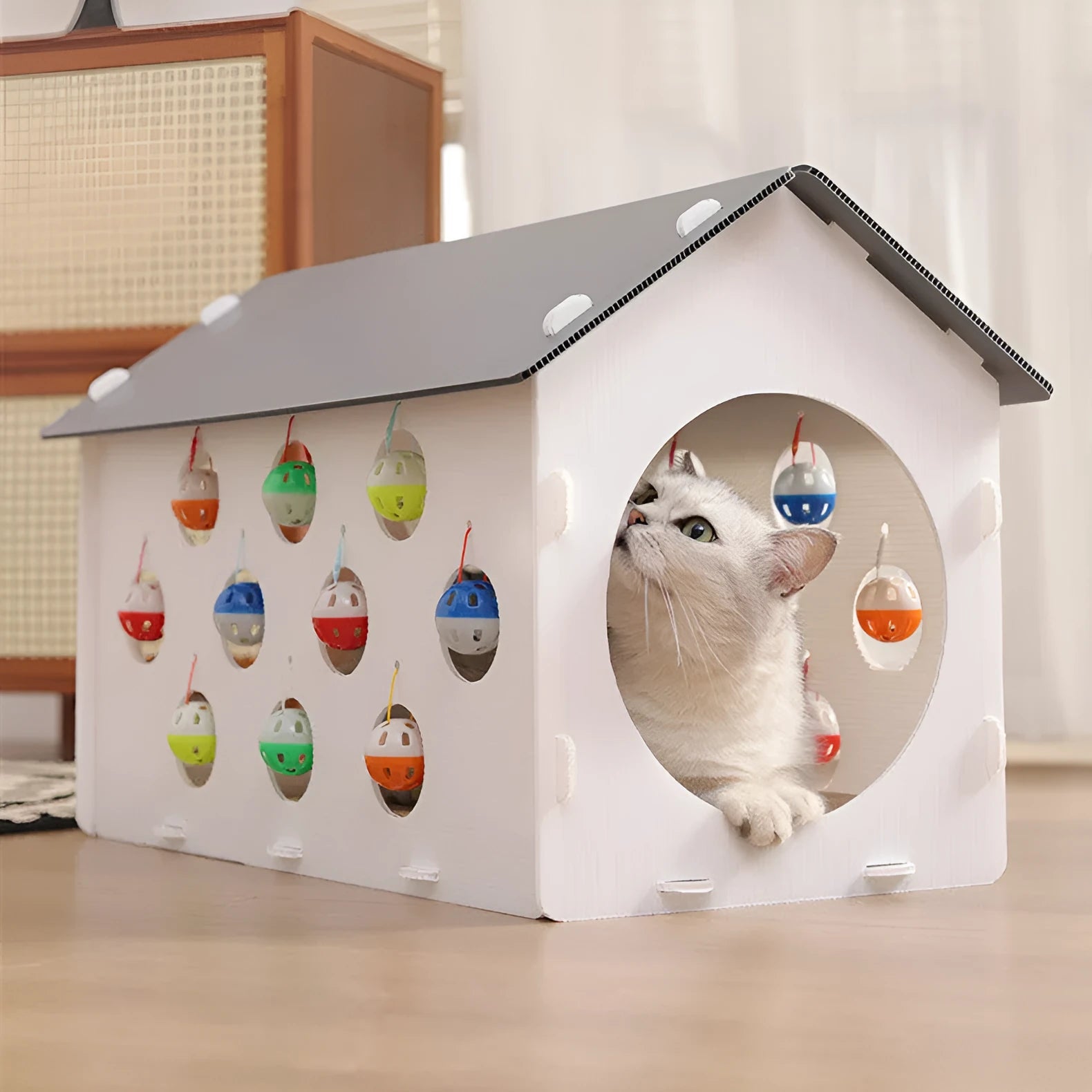 Durable plastic cat scratch board with an attached tunnel and a dangling bell ball toy on a neutral carpet.