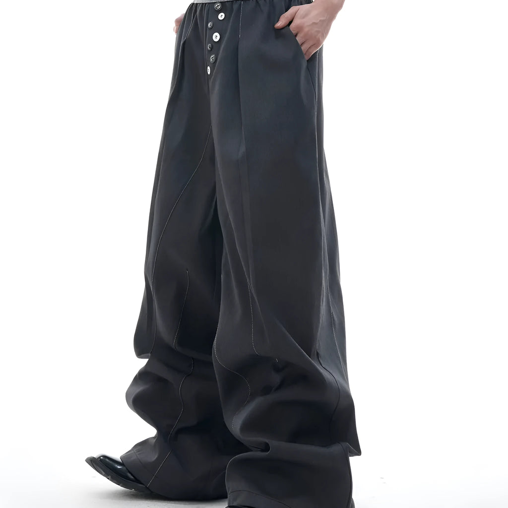 Straight-leg high-waisted trousers in black with a drooping waistband and button detail on a neutral background.