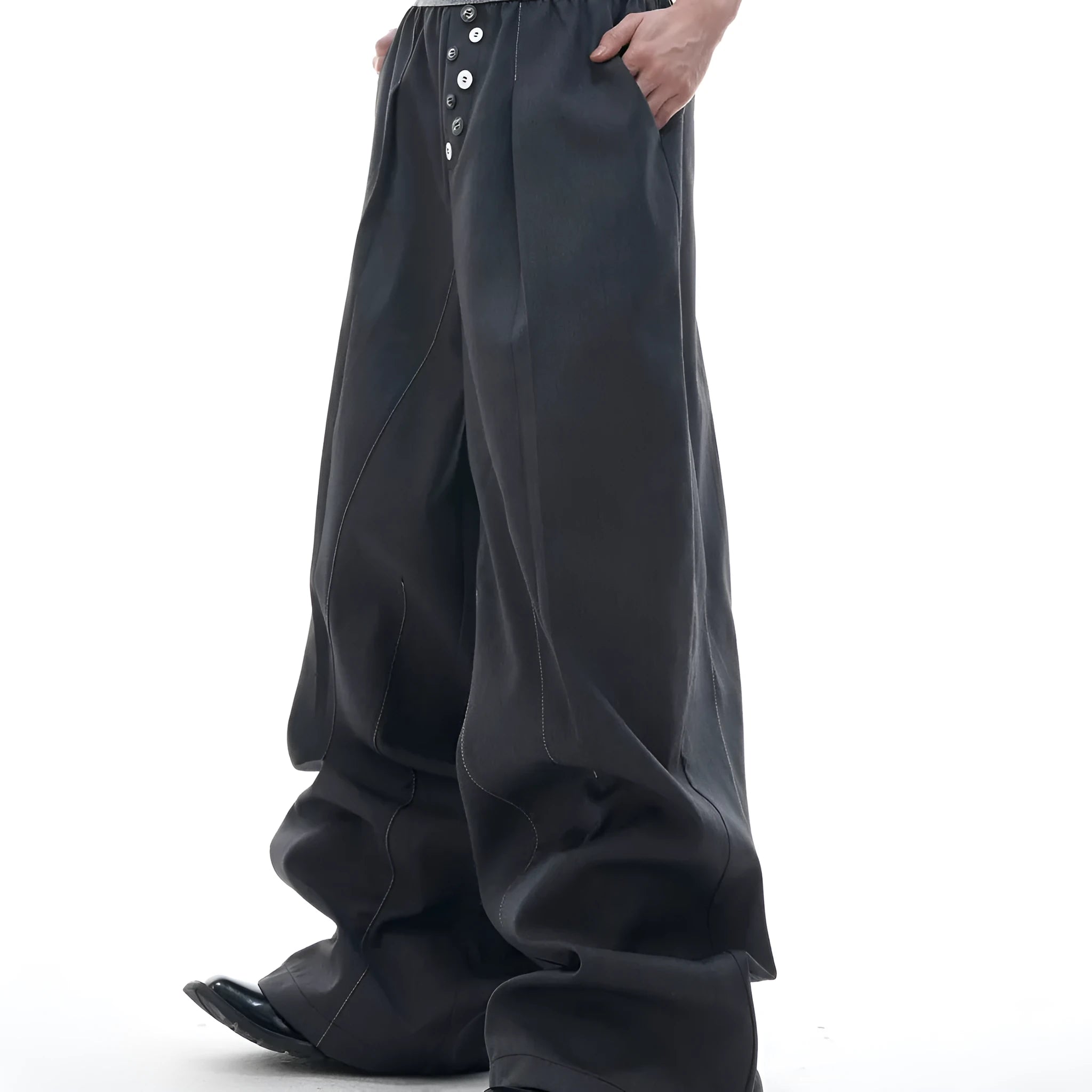 Straight-leg high-waisted trousers in black with a drooping waistband and button detail on a neutral background.
