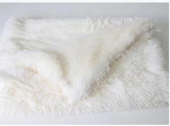 Soft grey long plush pet blanket for dogs on a wooden floor next to a kennel.
