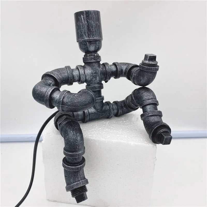 Industrial retro style iron pipe table lamp with water pipe robot design on a desk.