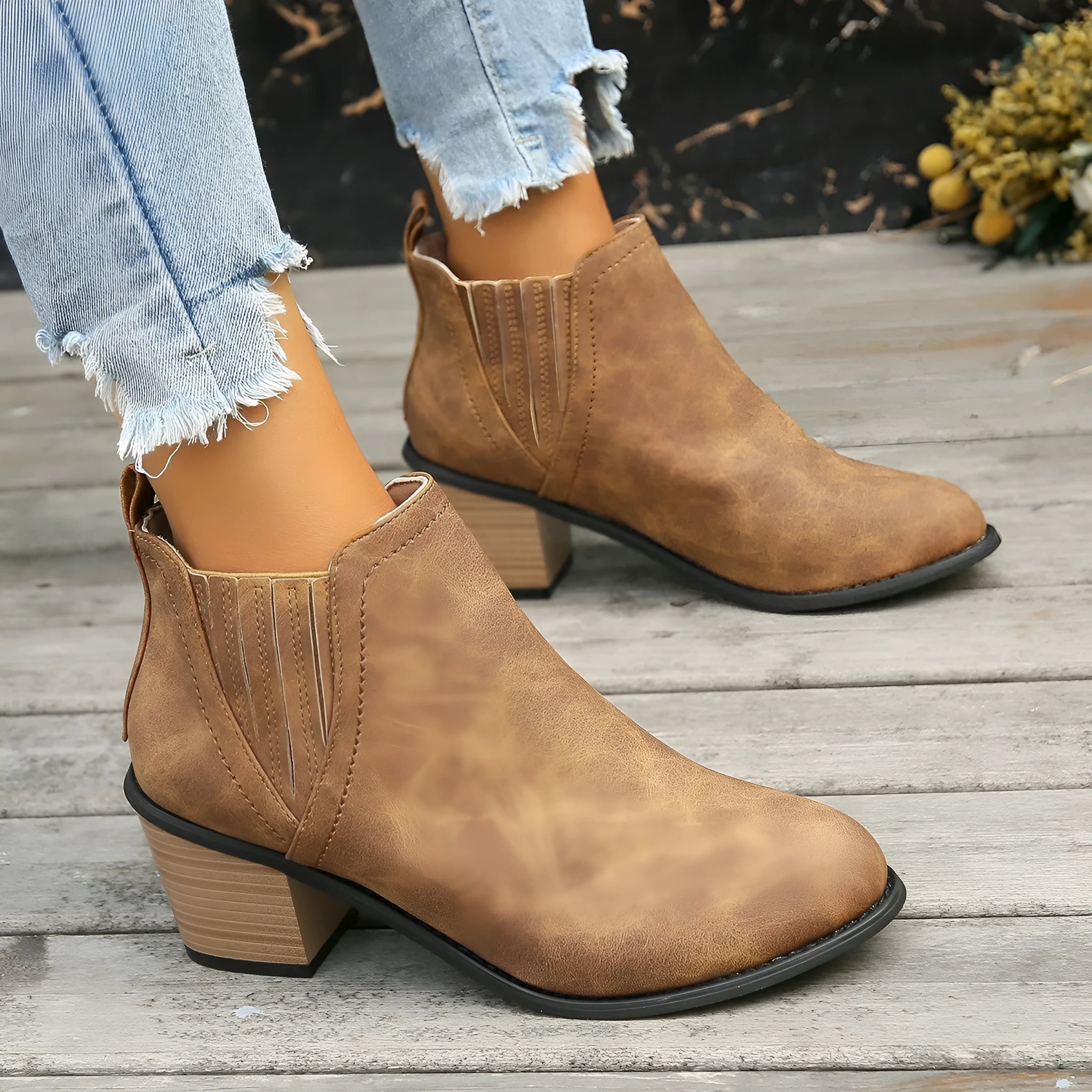 Women's black slip-on ankle boots with pointed toe and thick square heel on a wooden floor.