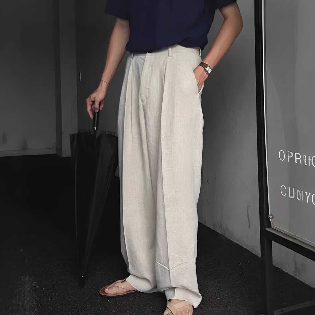 Men's apricot coloured wide-leg cotton linen trousers with a mid waist and zip fly on a neutral background.
