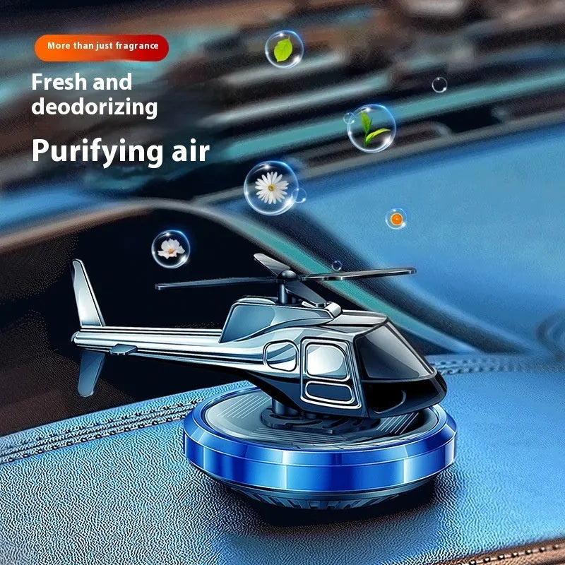 Silver metal solar-powered helicopter car air freshener rotating on a car dashboard.