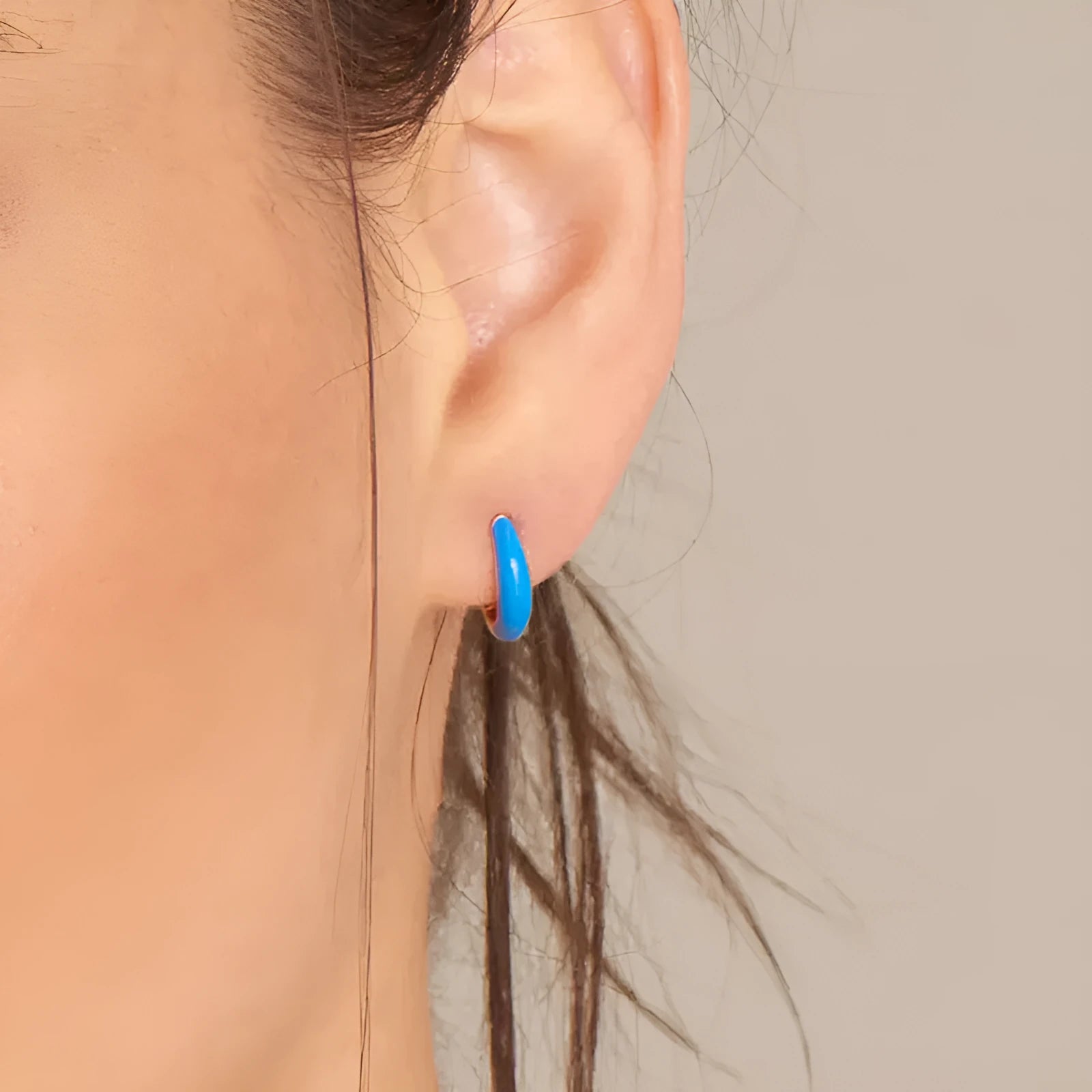 A pair of glossy light green epoxy oval earrings with a U-shaped curve and silver-coloured post on a grey background.