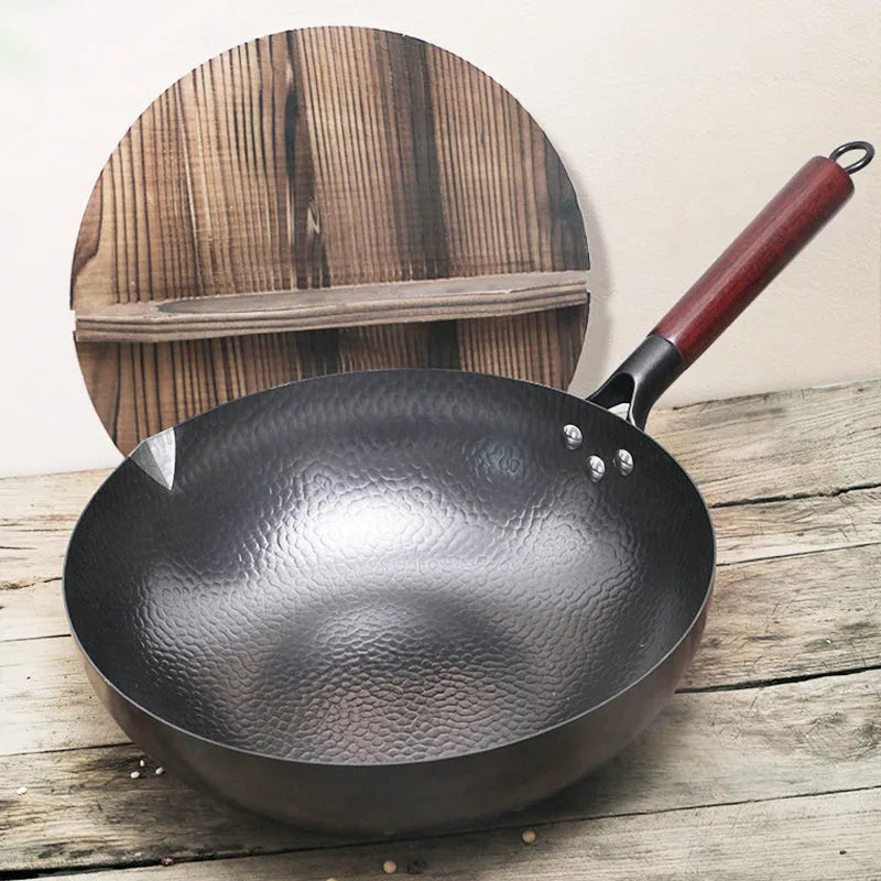 Black traditional cast iron wok with a long wooden handle on a kitchen counter.