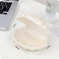 White porcelain scallop shell tray with optional warm LED night light, holding small jewellery on a bedside table.