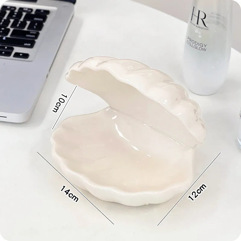 White porcelain scallop shell tray with optional warm LED night light, holding small jewellery on a bedside table.