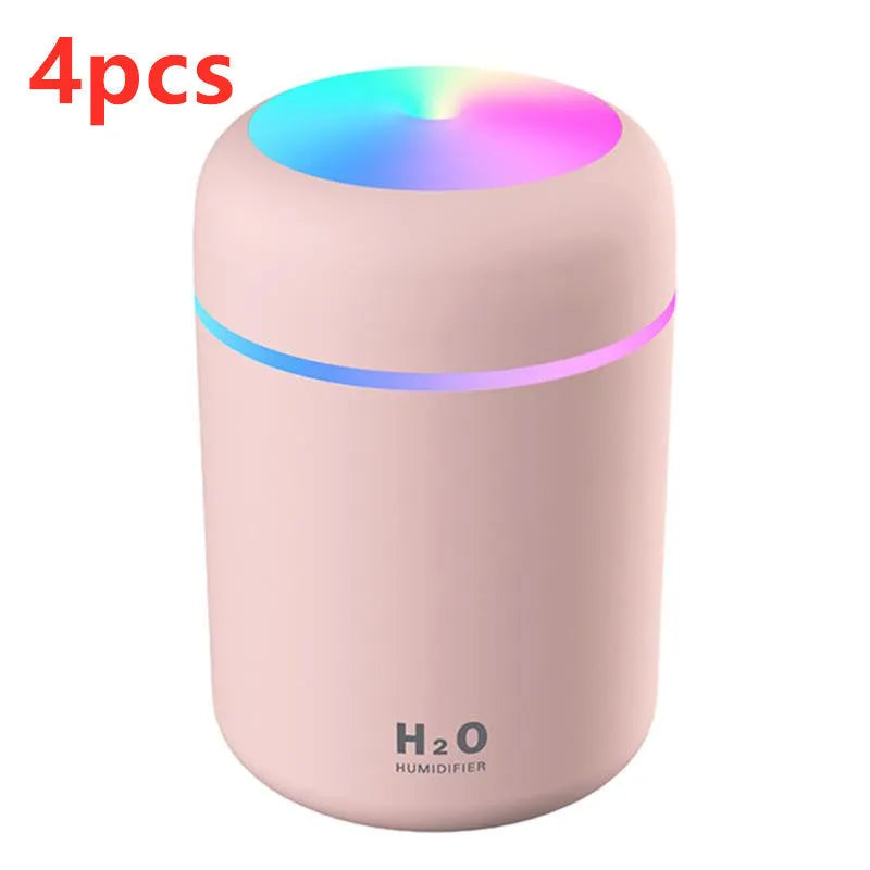 Pink USB mini humidifier with LED lights on wooden desk beside laptop