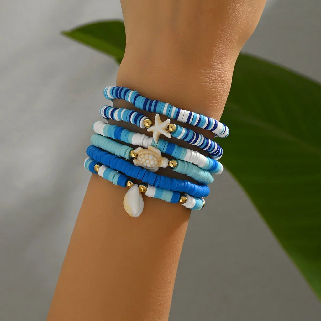 Six handmade Bohemian blue polymer clay bracelets with shell designs and geometric shapes arranged together