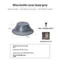 Beige plastic camping lantern shaped like a wine bottle with a glowing LED light inside on a wooden surface.