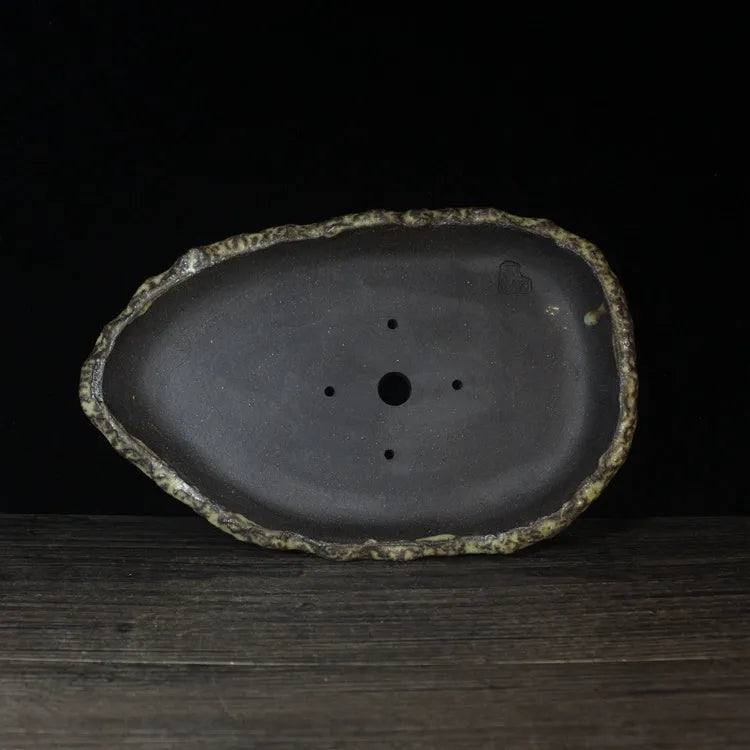 Handmade purple clay flower pot in a unique shape on a floor, showing colour and texture detail.